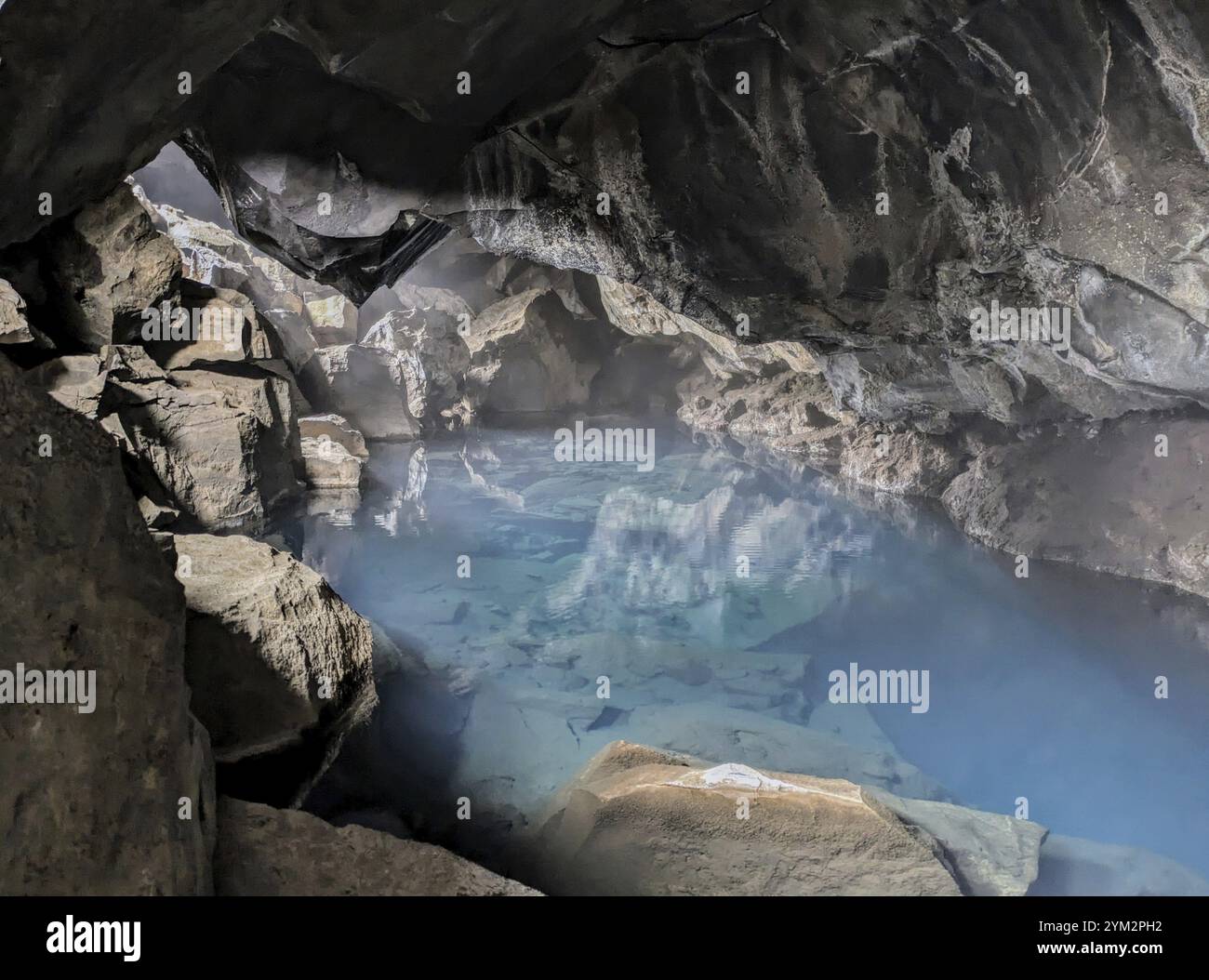 Geheimnisvolle Höhle mit einem ruhigen blauen Wasserpool und Reflexionen, umgeben von felsigem Inneren. Island Stockfoto