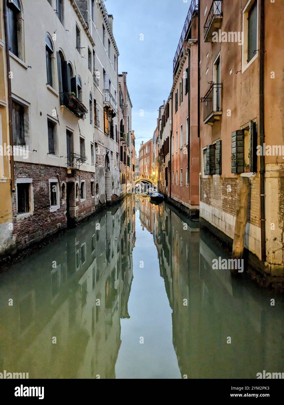 Ein ruhiger schmaler Kanal, flankiert von alten, eng gebauten Strukturen, die sich im Wasser spiegeln. Venedig, Italien, Europa Stockfoto