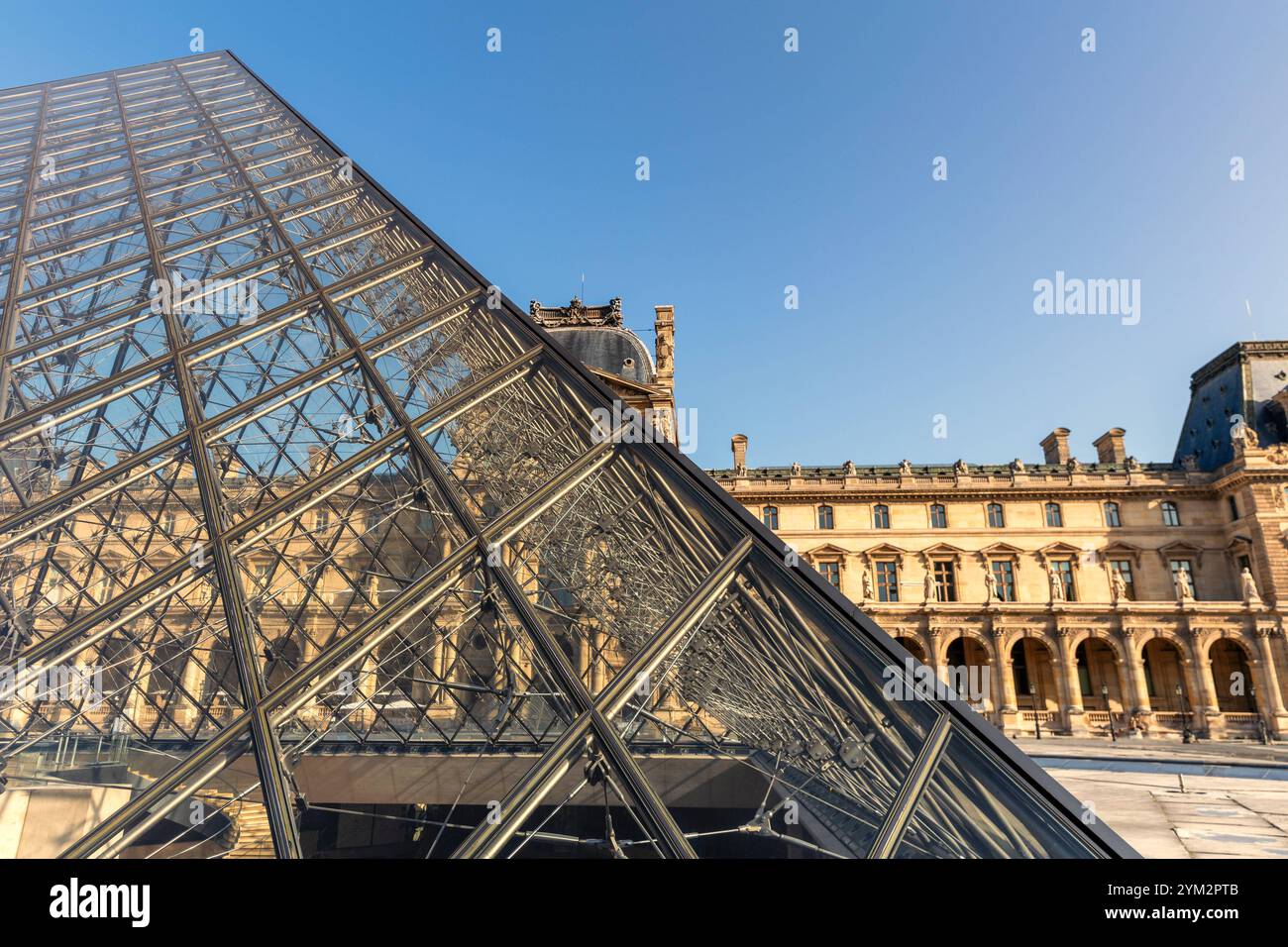 Eine faszinierende Aufnahme der Glaspyramide vor dem Louvre in Paris, Frankreich. Die moderne Architektur der Pyramide spiegelt die historischen Fassaden des Museumsgebäudes wider, während der klare blaue Himmel die harmonische Verbindung von Tradition und Moderne unterstreicht. Die Szene ist in warmes Sonnenlicht taucht, das die Strukturen und Details hervorhebt. *** Ein faszinierendes Bild der Glaspyramide vor dem Louvre in Paris, Frankreich die moderne Architektur der Pyramide spiegelt die historischen Fassaden des Museumsgebäudes wider, während der klare blaue Himmel das harmonische miteinander unterstreicht Stockfoto