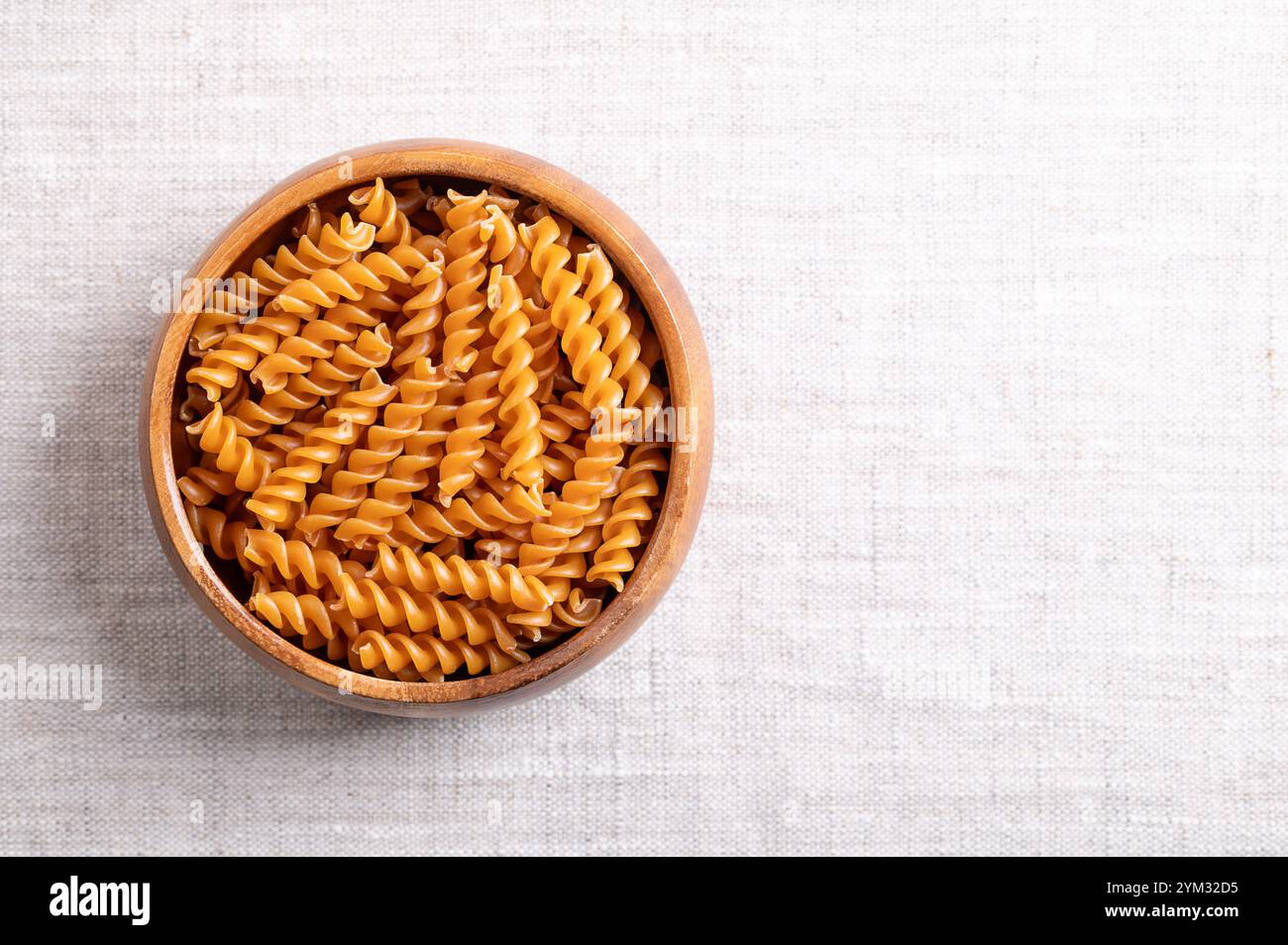 Kichererbsen-Spiralnudeln in einer Holzschale, mit leerem Platz für Text. Kleine Fusilli, eine Nudelsorte in Spiralform oder Korkenzieher-Form. Stockfoto