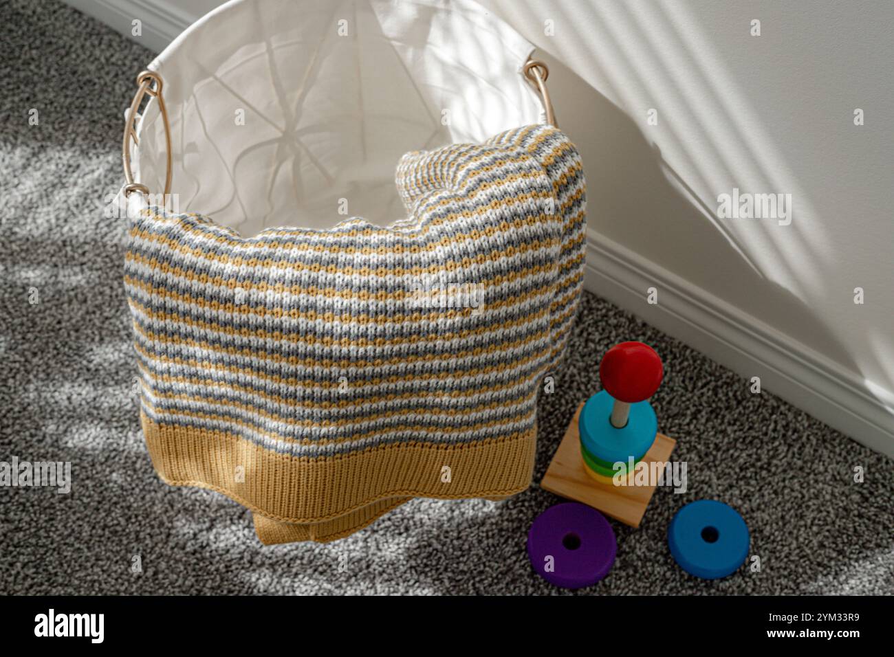Ein Korb voller gestrickter Gegenstände, darunter eine gestreifte Decke und ein Teddybär. Der Korb wird auf einen Teppichboden gestellt Stockfoto