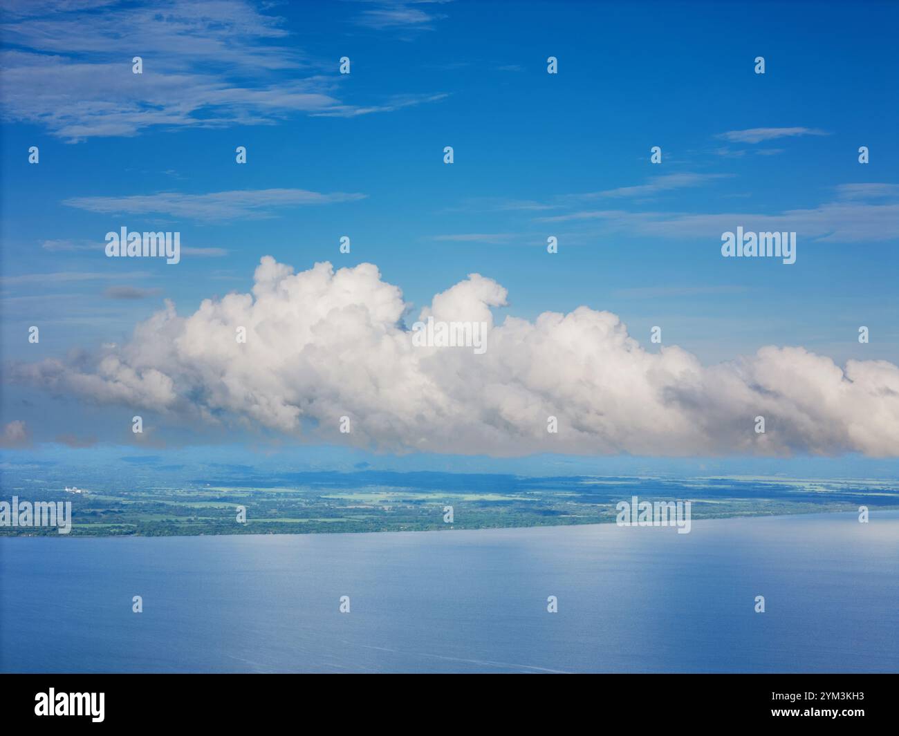 Flauschige weiße Wolken schweben über dem ruhigen Ozean und reflektieren den klaren blauen Himmel während des friedlichen Tages. Stockfoto