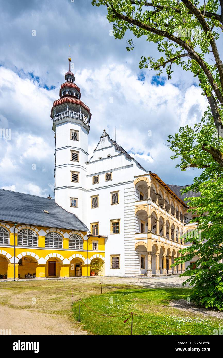 Der Innenhof des Velke Losiny Chateau bietet eine beeindruckende architektonische Mischung mit seinem kunstvollen Turm, lebhaften Farben und üppigem Grün, alles beleuchtet von einem sonnigen, teilweise bewölkten Tag. Stockfoto