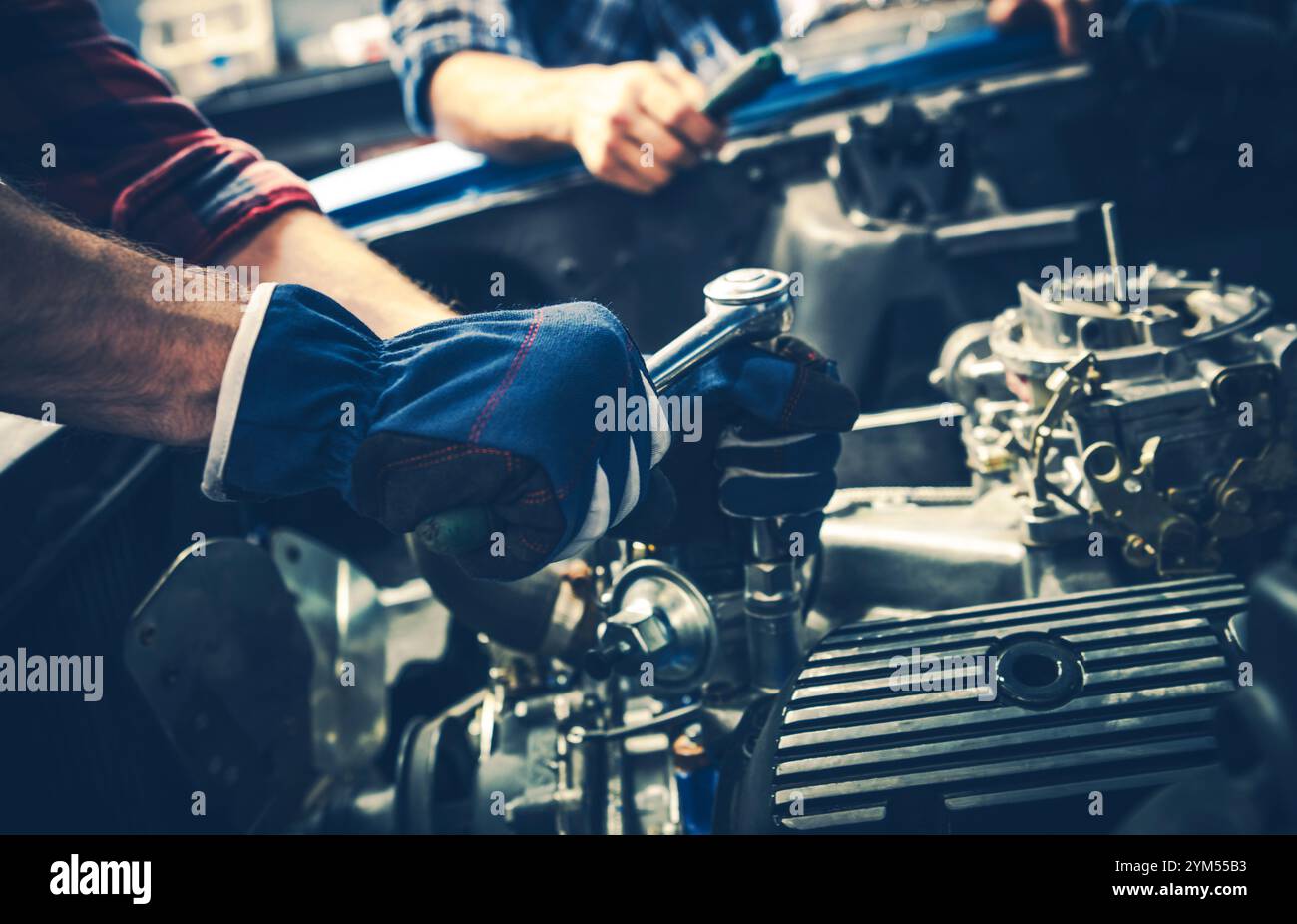 Zwei Mechaniker konzentrieren sich auf die Reparatur eines Automotors, wobei sie bei Tageslicht verschiedene Werkzeuge für die Aufgabe in einer gut ausgestatteten Werkstatt verwenden. Stockfoto