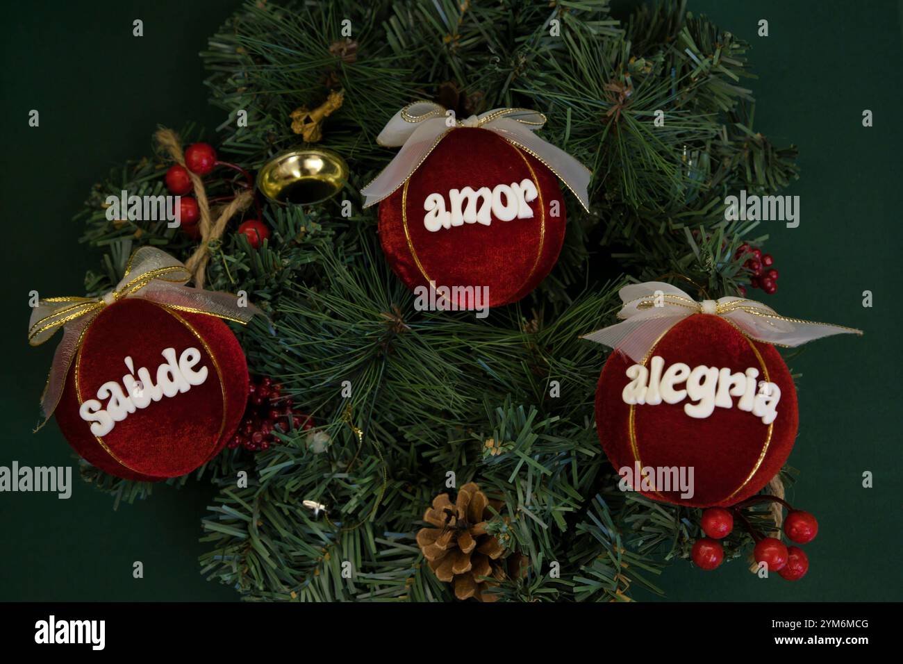 Drei rote Kugeln mit weißer Schrift darauf. Die Schrift ist auf Portugiesisch und sagt: "Saude, Amor, Alegria." Die Kugeln werden auf einem Weihnachts t platziert Stockfoto