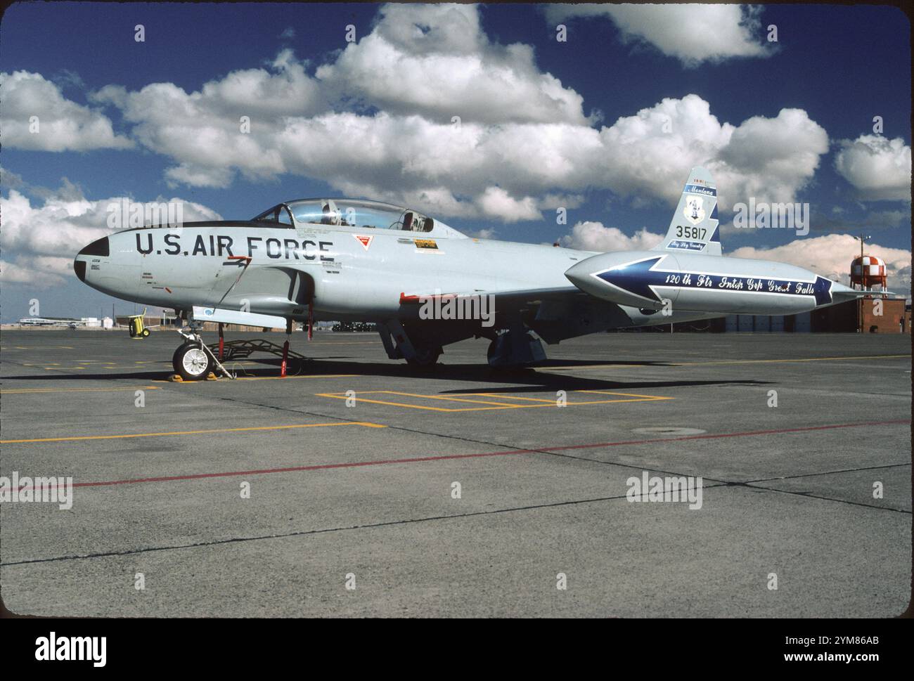 Montana ANG 120th Fighter Interceptor Group T-33A auf der ANG-Rampe am Great Falls IAP an einem typischen sonnigen Tag. Klare Leitungen von T-33 fallen heraus. Trinktanks waren eine Notwendigkeit, da die Rumpftankkapazität gegenüber dem P-80 für das hintere Cockpit reduziert wurde. Lockheed selbst finanzierte T-33-Entwicklung, da die Zahl der tödlichen Unfälle bei P-90 zu hoch war. Die Piloten hatten Schwierigkeiten, die T-33 zu landen, da sie nicht schnell langsamer wurden wie die Propellerjäger, die sie gewohnt waren. Auch die Motorreaktion bei einer gebremsten Landung im Leerlauf war zu langsam. Beachten Sie die Geschwindigkeitsbremsen und Klappen unter Rumpf und Tragflächen. Stockfoto