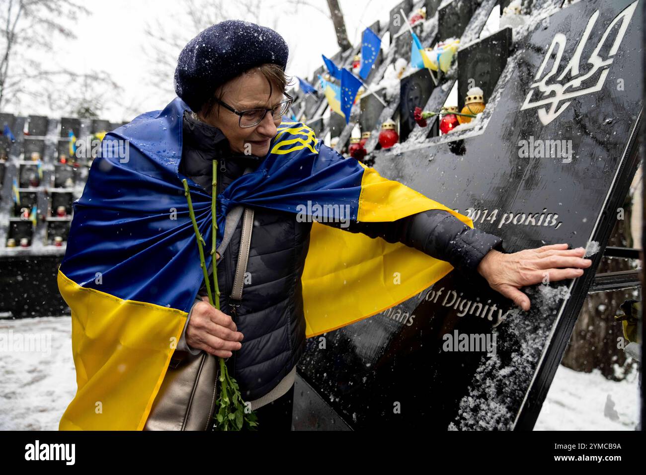 Eine Frau, die in ukrainische Flagge gehüllt ist, reinigt die Himmlischen Hundred Helden-Gedenkstätte aus frischem Schnee beim Gedenken an den Tag der würde und Freiheit. Es wird ein interreligiöses Gebet für die Ukraine und ihre Freiheitskämpfer und eine Zeremonie zu Ehren gefallener Verteidiger abgehalten. Der Tag der würde erinnert an zwei Schlüsselmomente der ukrainischen Geschichte, die Orangene Revolution von 2004 und die Revolution der würde von 2013. Kiew Stadt *** Frau in ukrainische Flagge gehüllt, die das Himmlische Hundred Helden-Denkmal vom Neuschnee reinigt, anlässlich des Tages der würde und Freiheit ein interreligiöses Gebet für U Stockfoto