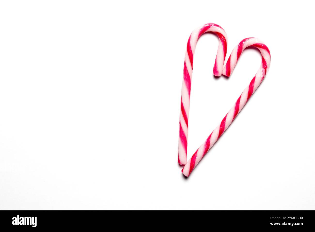 Zwei Zuckerstangen sind kreativ positioniert, um eine Herzform zu bilden, die Freude und Festlichkeit während der Weihnachtszeit repräsentieren. Stockfoto