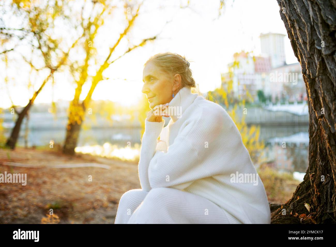 Frau in weißem Pullover, die im Herbst am Fluss sitzt Stockfoto