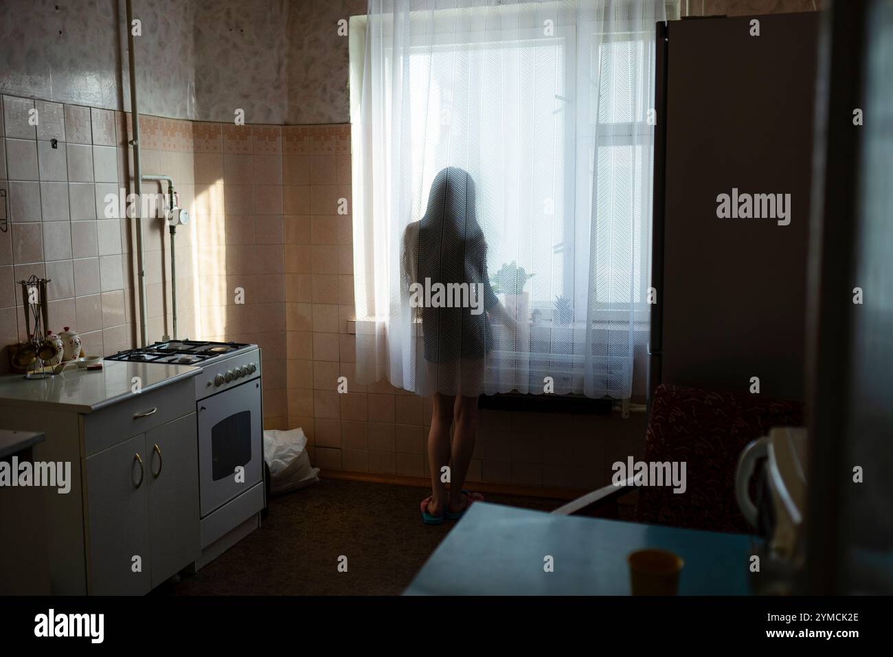 Rückansicht einer Frau, die durch das Fenster in der Küche schaut Stockfoto