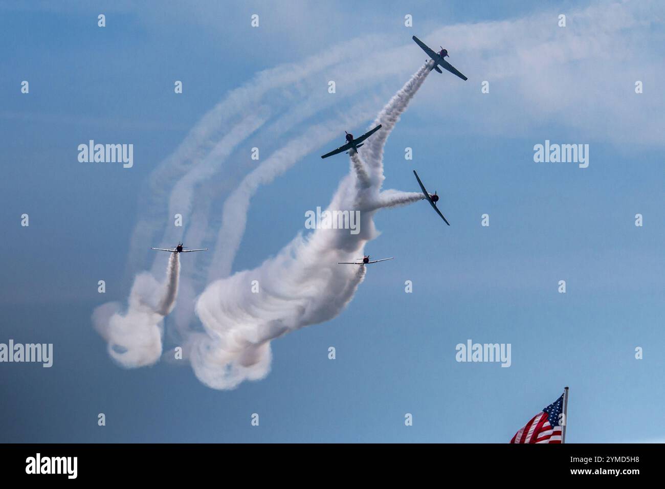 Drei Stuntflugzeuge führen enge Manöver durch und hinterlassen leuchtende Rauchspuren unter einem klaren blauen Himmel. Stockfoto