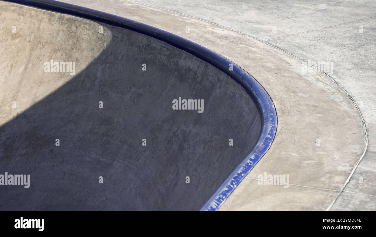 Eine geschwungene Skateboardschale mit glatter Oberfläche und schattigen Kanten befindet sich in einem urbanen Skatepark bei hellem Tageslicht. Stockfoto