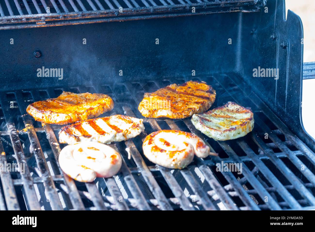 Mariniertes Schweinefleisch- und Hühnchensteak auf dem Grillrost mit Flammen. Hochwertige Fotos Stockfoto