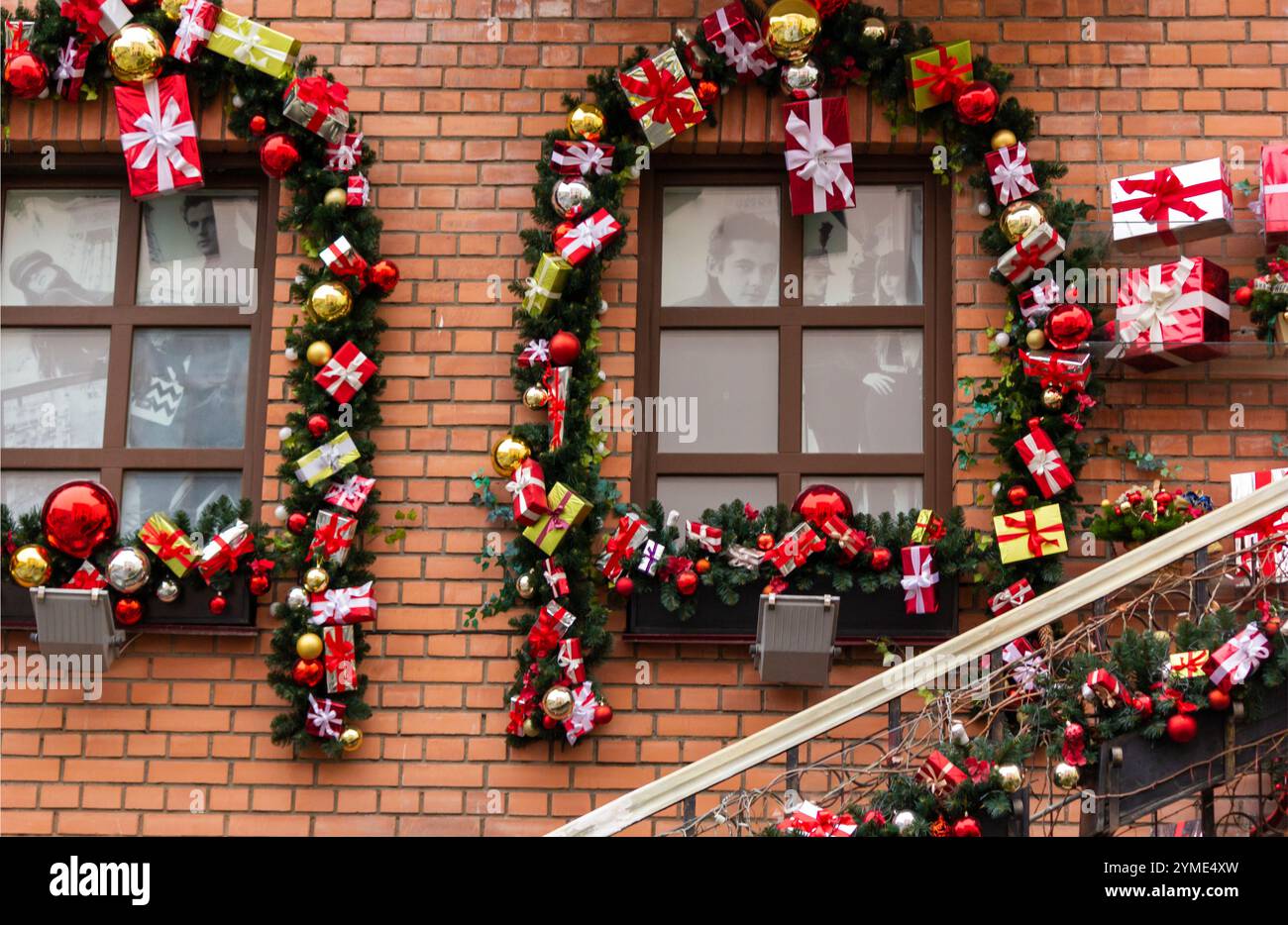 Die Fenster des Hauses sind weihnachtlich dekoriert. Weihnachtliche Einrichtung im Freien mit künstlichem Weihnachtsbaum und roten Kugeln mit Kisten Stockfoto