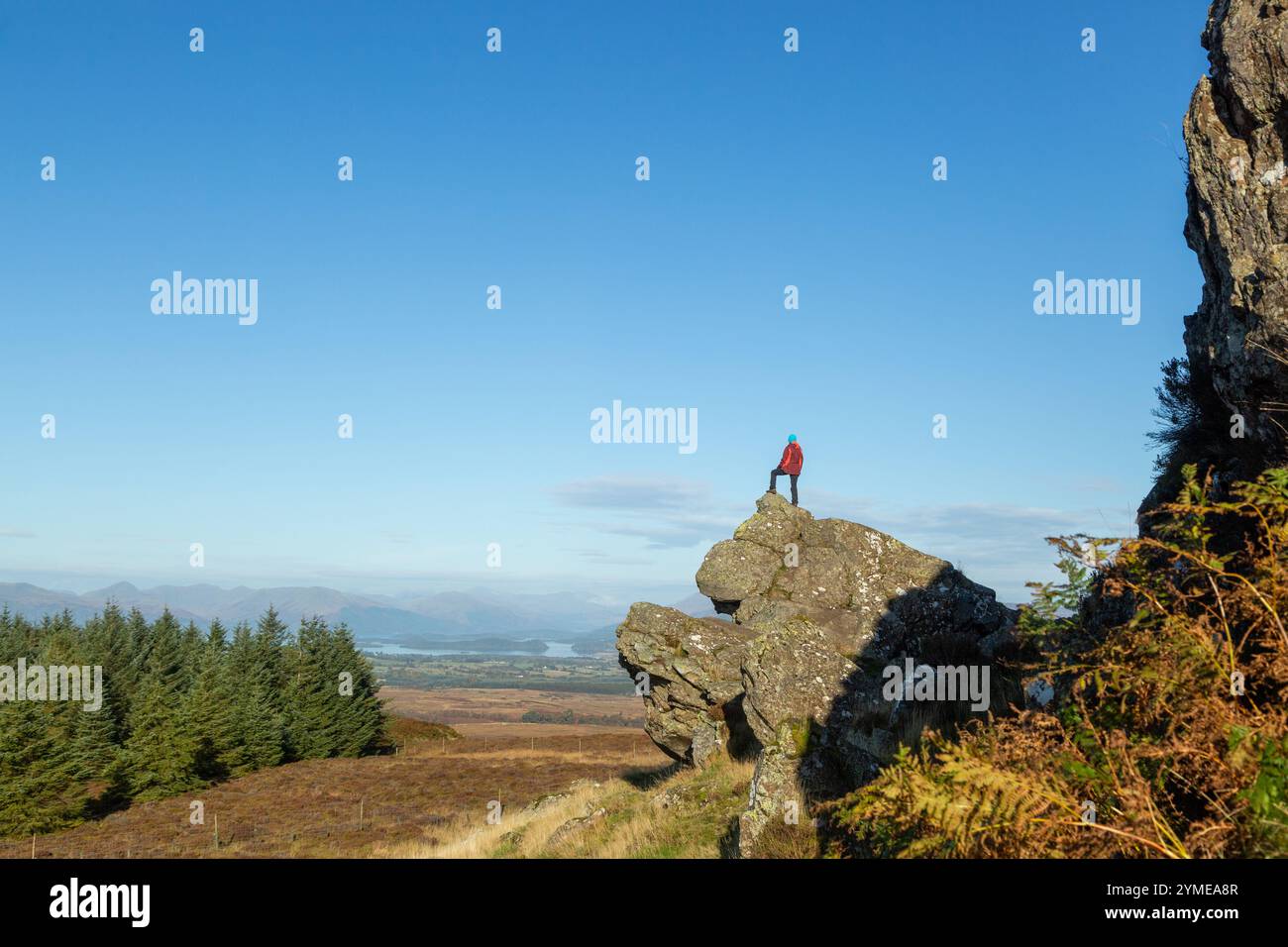 Eine Person, die auf einem Felsen mit Blick auf Loch Lomond in der Nähe des Whangie, Auchineden Hill, Schottland, steht. Stockfoto