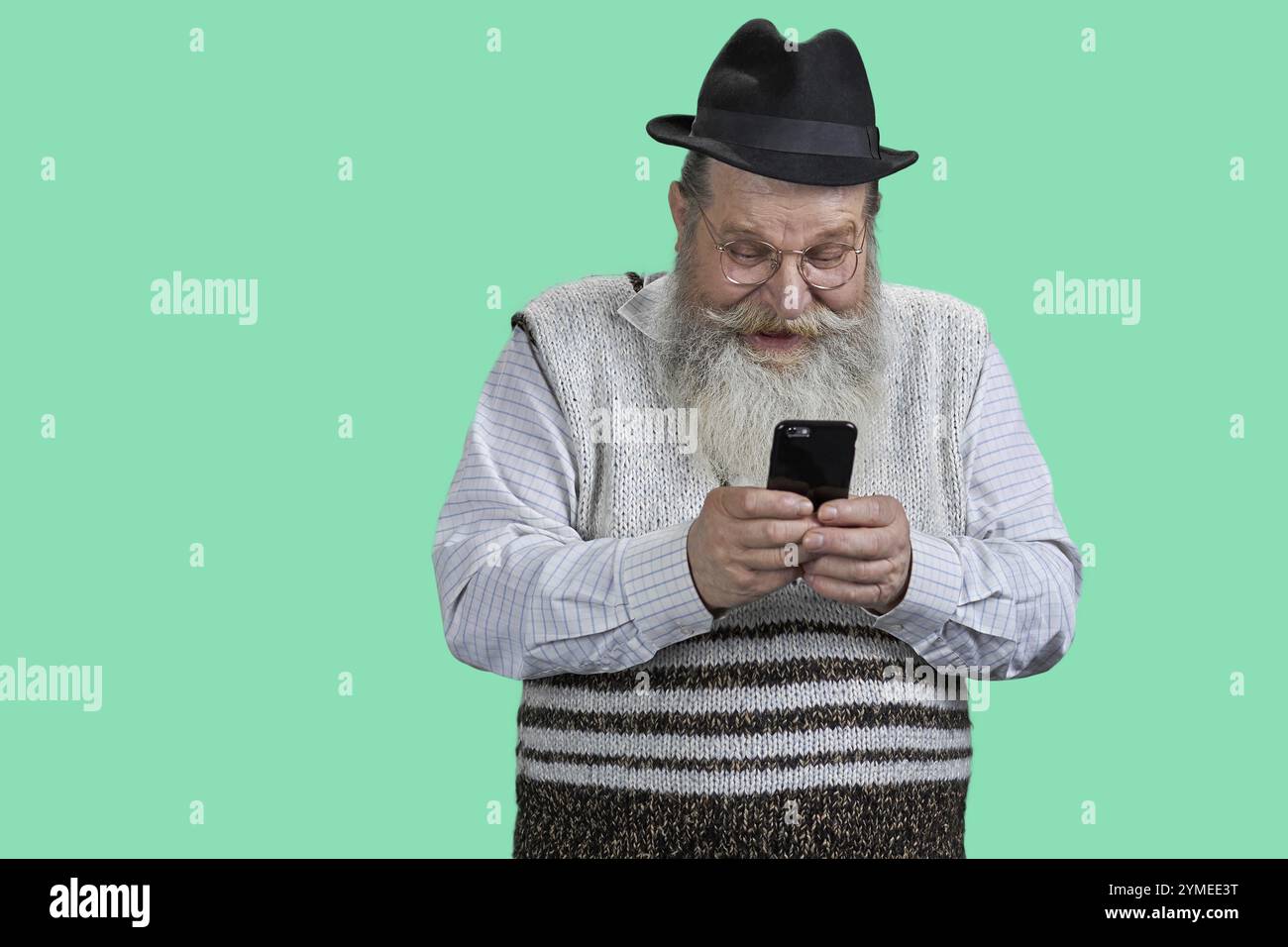 Porträt eines engagierten älteren Mannes, der das Telefon in zwei Händen hält. Isoliert auf lebhaftem grünem Hintergrund Stockfoto