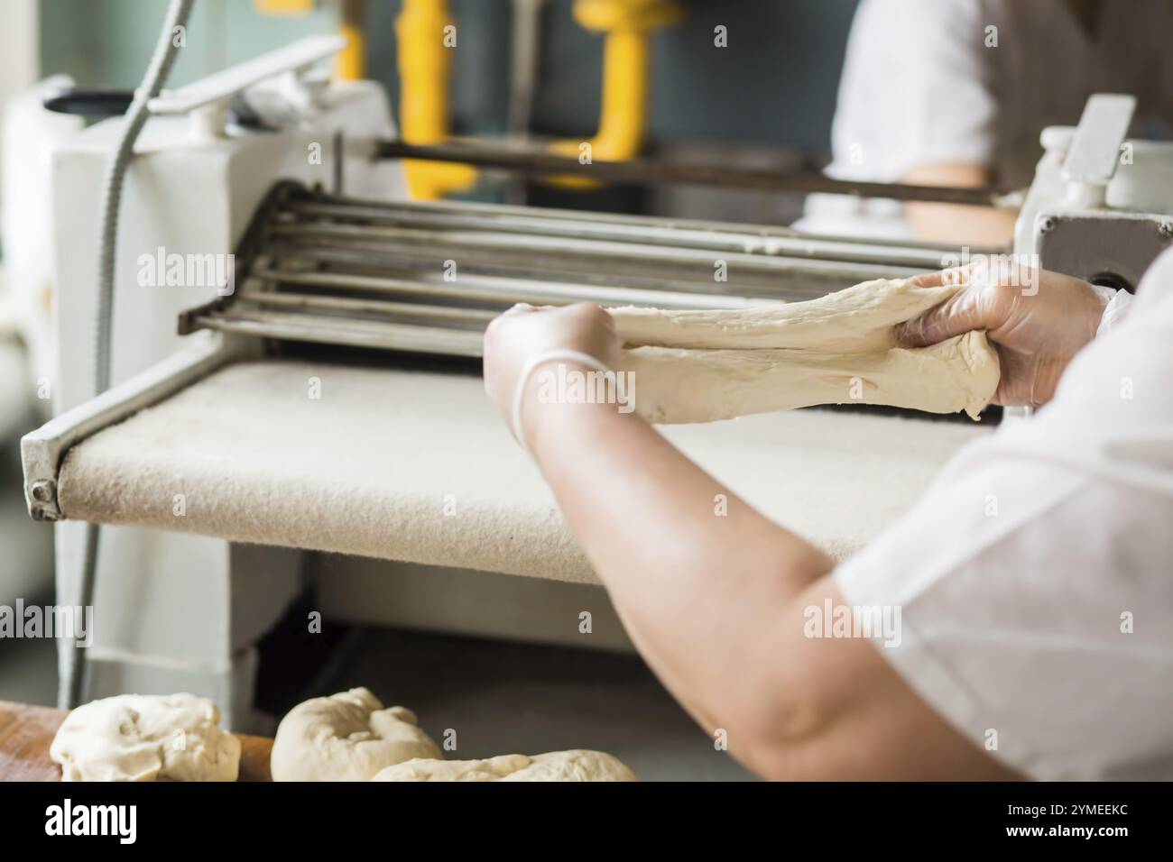 Bäckerin, die in der Bäckerei mit Teig arbeitet. Backwarenförderer im Hintergrund. Konditorei in der Lebensmittelfabrik Stockfoto