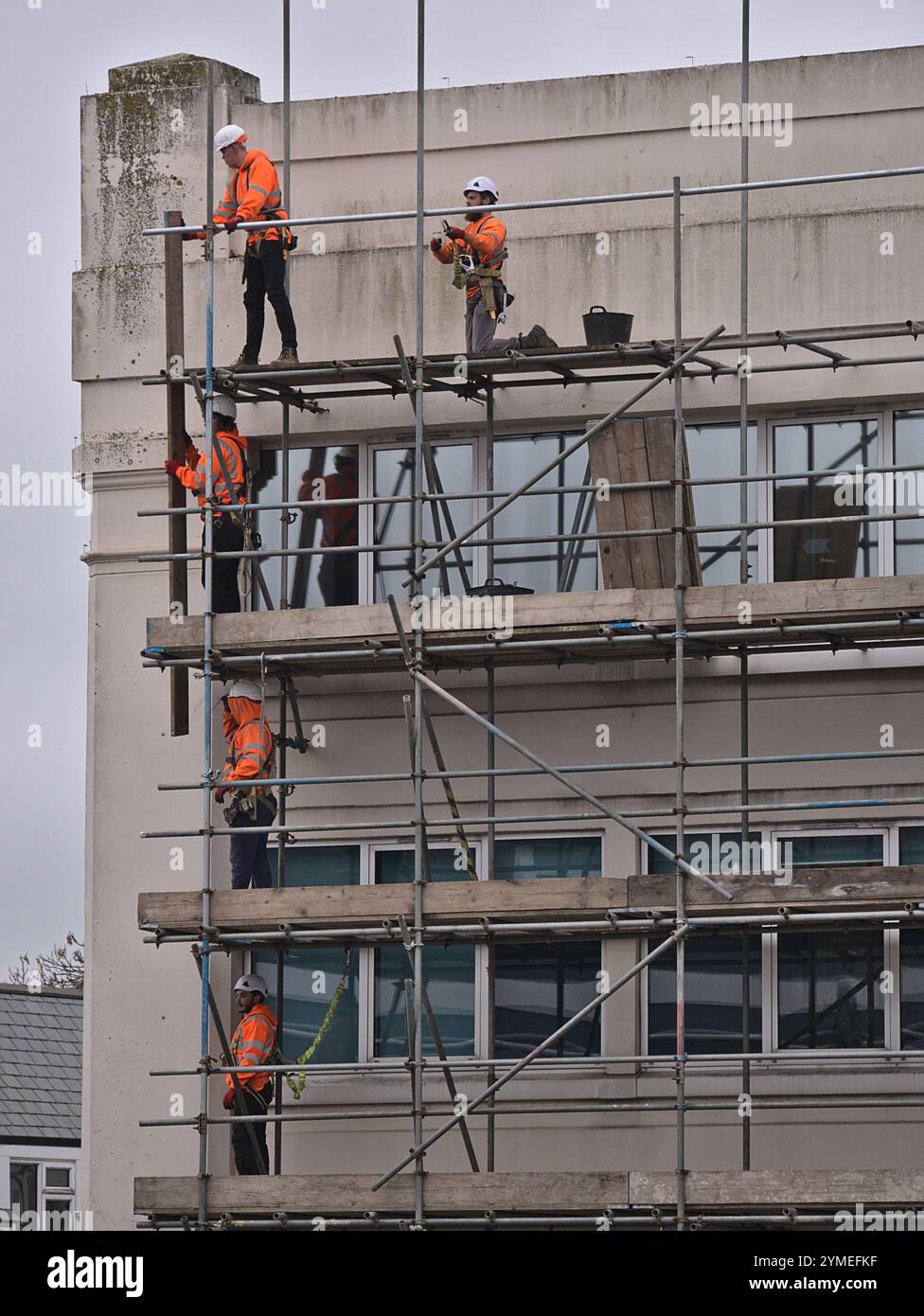 Gerüste werden von einem Team von Gerüstbauern in orangefarbenen Hi-Vis und Schutzhelmen errichtet, die gemeinsam Gerüstbretter auf die obere Plattform heben Stockfoto