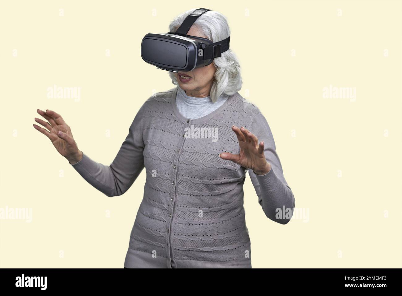 Eine ältere Frau mit Virtual-Reality-Headset ist von der VR-Erfahrung beeindruckt. Alte Frau mit vr-Brille auf hellgelbem Hintergrund. Neue Technologien und Stockfoto