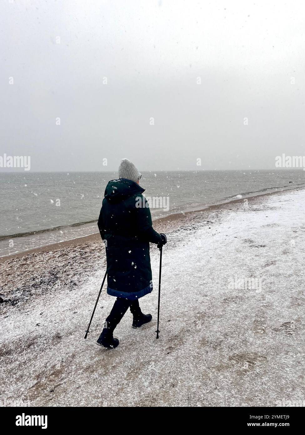 Einsame Seniorin, die an einem kalten Wintertag an der Ostseeküste in Danzig, Polen, Europa entlang des schneebedeckten Strandes von Danzig spaziert - Smartphone-aufgenommenes Stockfoto