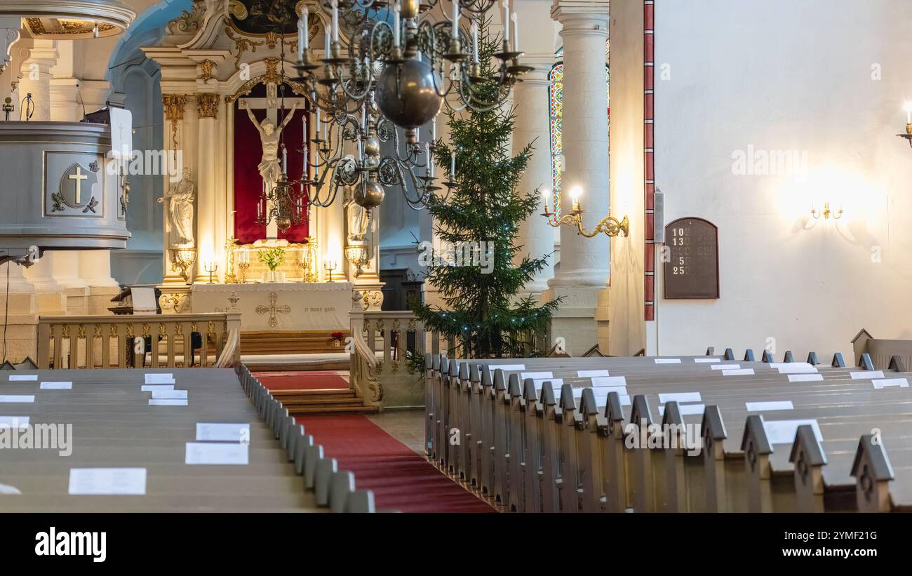 Gemütliches Inneres einer Domkathedrale in Riga, Lettland, mit einem Weihnachtsbaum neben dem Altar dekoriert. Warmes Kerzenlicht und kunstvolle Kronleuchter sorgen für einen Stockfoto