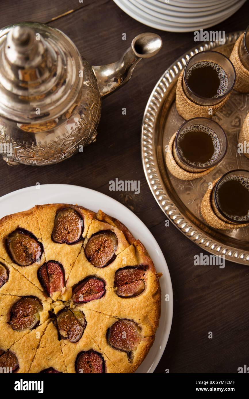 Traditioneller marokkanischer Tee mit Feigenkuchen, serviert auf einem rustikalen Holztisch mit kunstvollen Details, kultureller Authentizität und süßem Genuss. Stockfoto