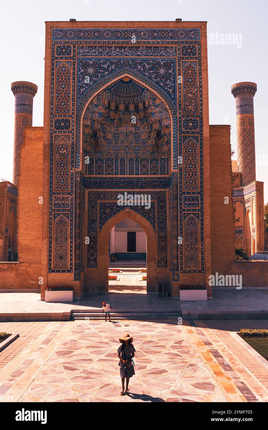 Zwei Kinder werden bei einem Spaziergang aus dem großen Amir Temur Mausoleum in Usbekistan an einem hellen sonnigen Tag gefangen. Der prächtige bogenförmige Eingang flankiert B Stockfoto