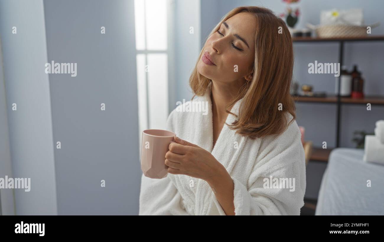 Junge Frau, die eine entspannende Pause in einem Wellness-Spa genießt und Kaffee trinkt, während sie im Haus ruhig und zufrieden aussieht. Stockfoto