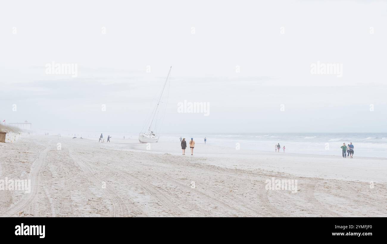 Vielfältige Gruppenwanderung am Sandy Beach mit Segelboot im Hintergrund, Wolkenkratzer Jacksonville, Florida, USA 03.15.2024 Stockfoto