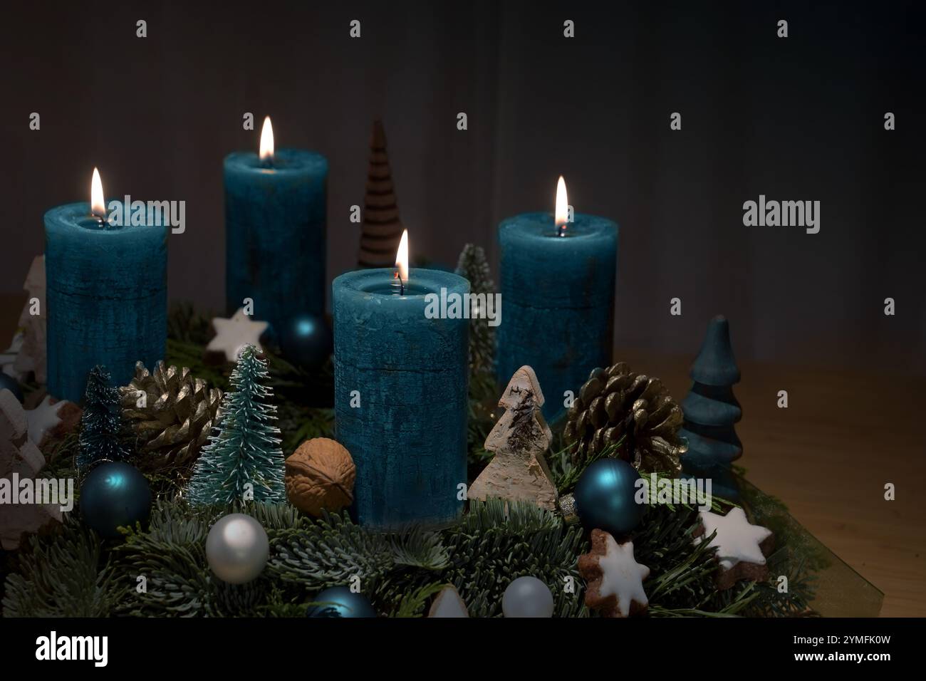 Vierter Advent, vier blau brennende Kerzen auf einem Kranz mit Weihnachtsdekoration vor dunklem Hintergrund mit Kopierraum, ausgewähltem Fokus, schmale Tiefe Stockfoto