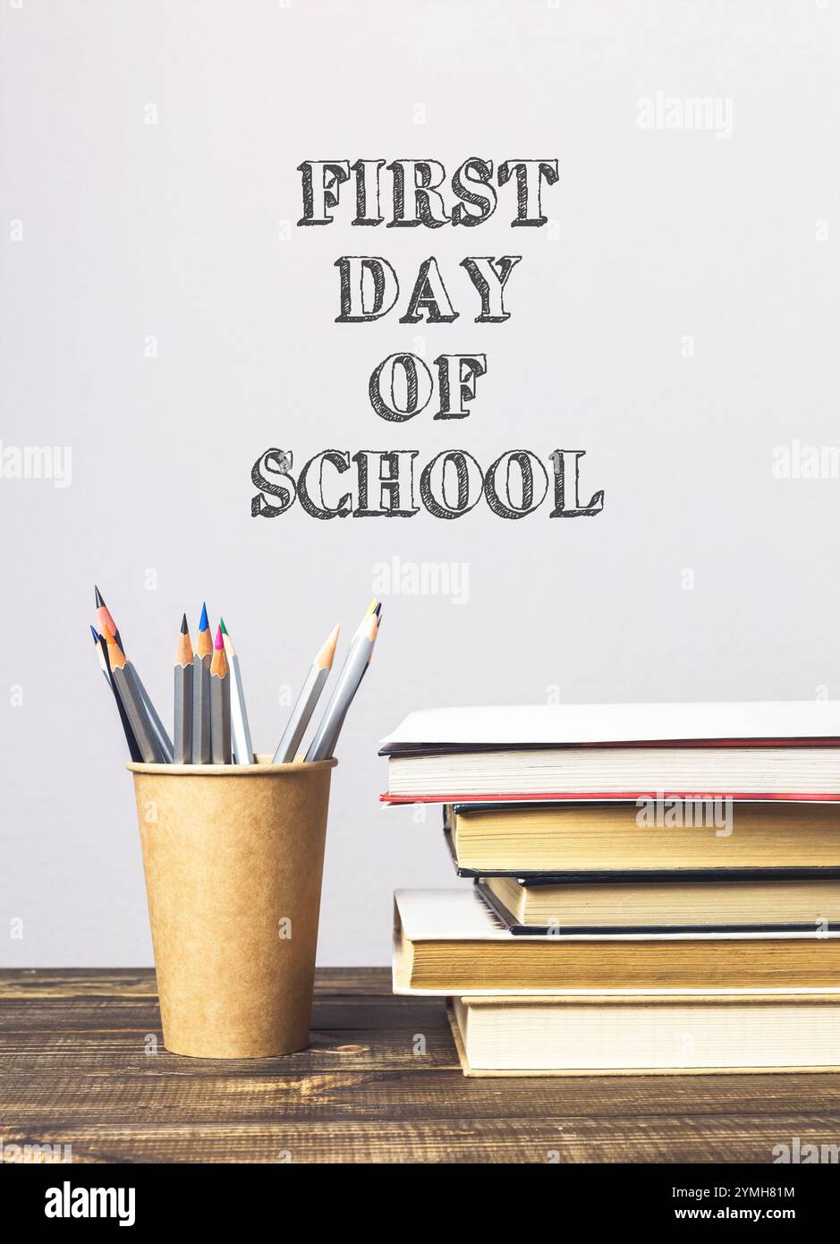 Ein Stapel Bücher und ein Bleistifthalter auf einem Tisch mit den Worten „erster Schultag“ hinter ihnen Stockfoto