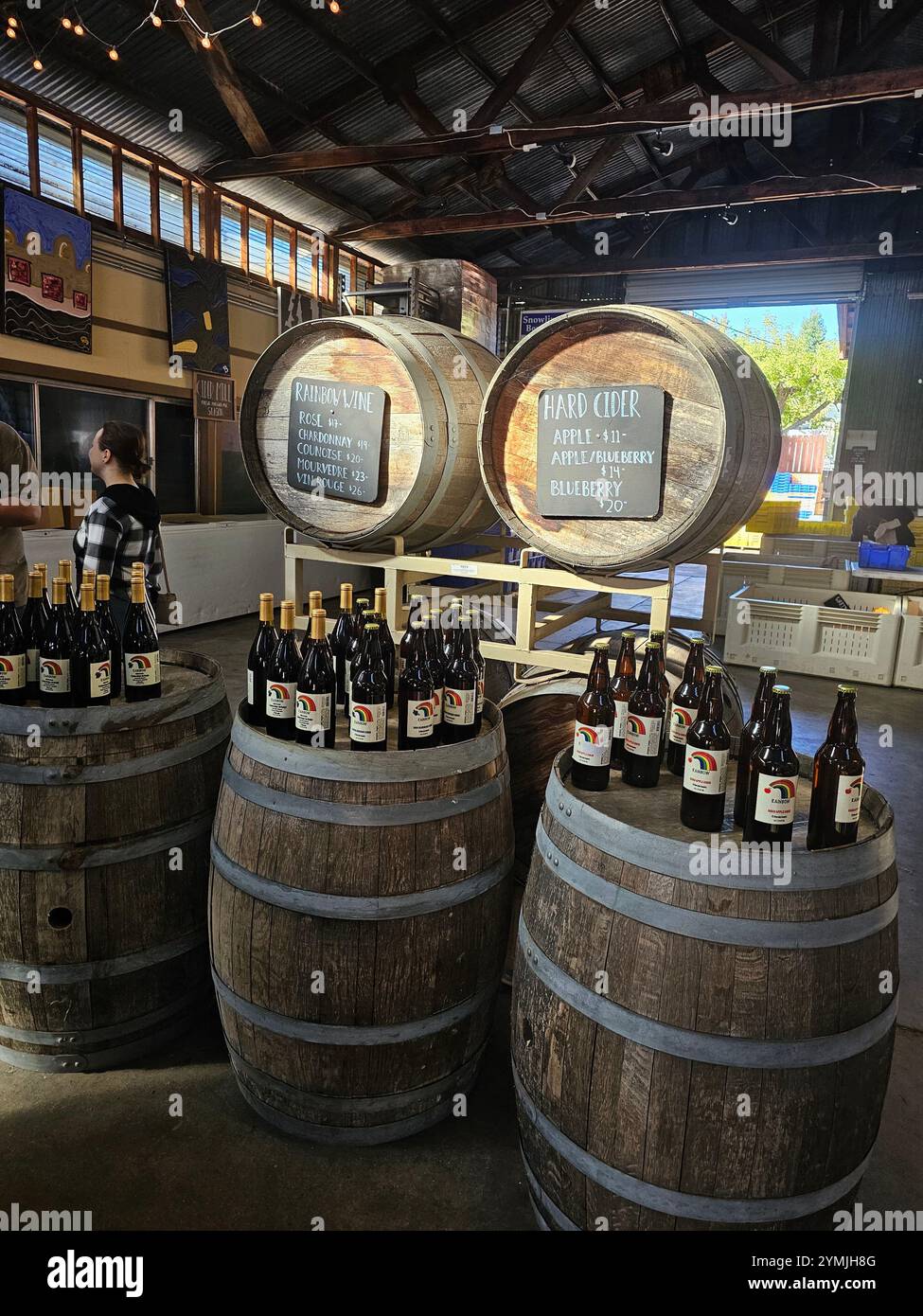 Rustikales Weingut mit Holzfässern, beschrifteten Flaschen Wein und Apfelwein und gemütlicher Beleuchtung. Perfekt für Themen der Weinbereitung. Stockfoto