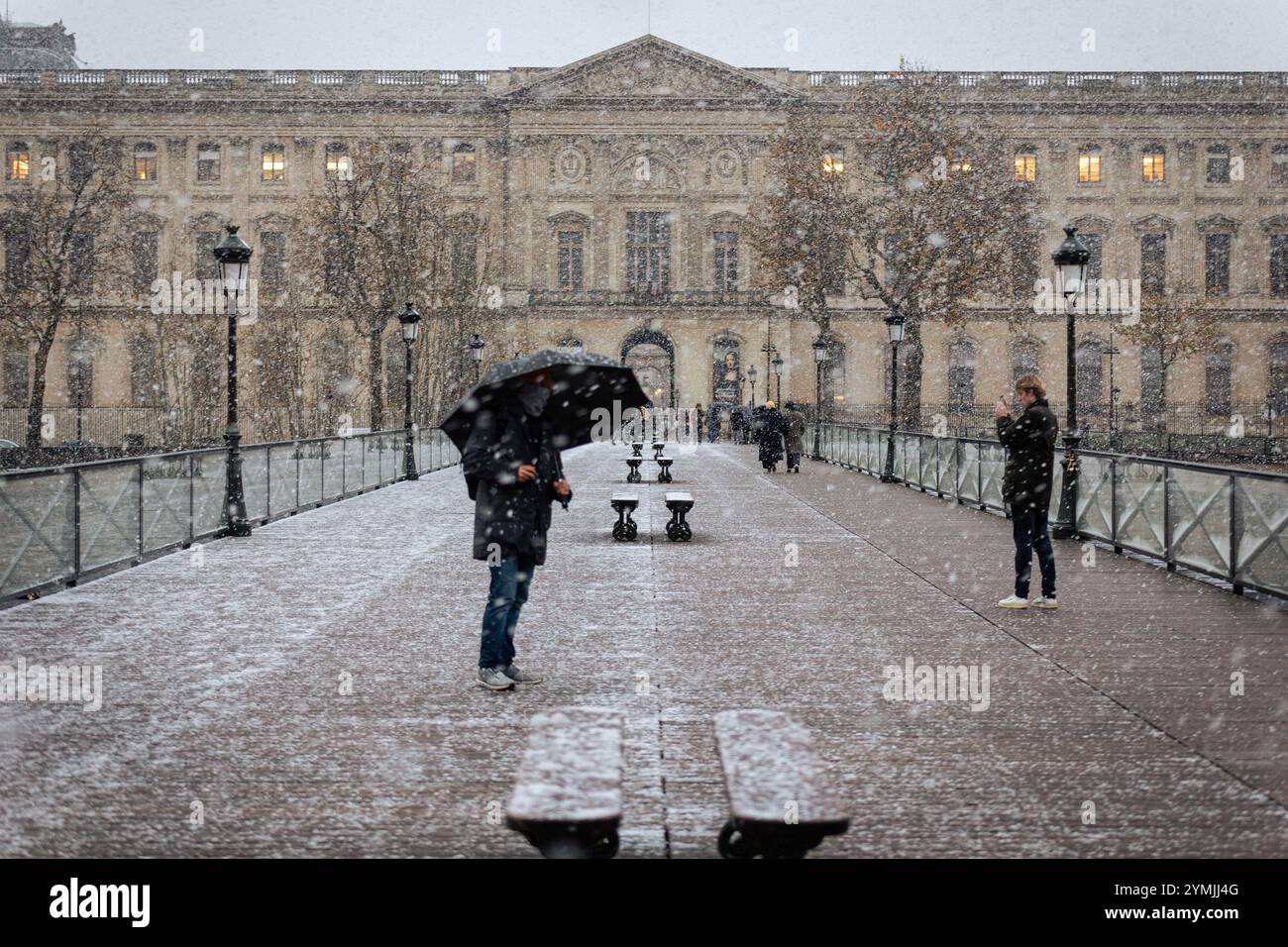 Paris, Frankreich. November 2024. Während des Schneefalls des Sturms Caetano spazieren die Menschen auf der Brücke der Künste neben dem Louvre-Palast. Der Sturm Caetano erreichte die Region Paris mit Schneefall, der im November 56 Jahre lang nicht mehr zu sehen war, mit 4 Zentimetern Schnee auf den Straßen der französischen Hauptstadt. Météo-France hat 38 Departements in Frankreich in den Status Orange gesetzt. Quelle: SOPA Images Limited/Alamy Live News Stockfoto