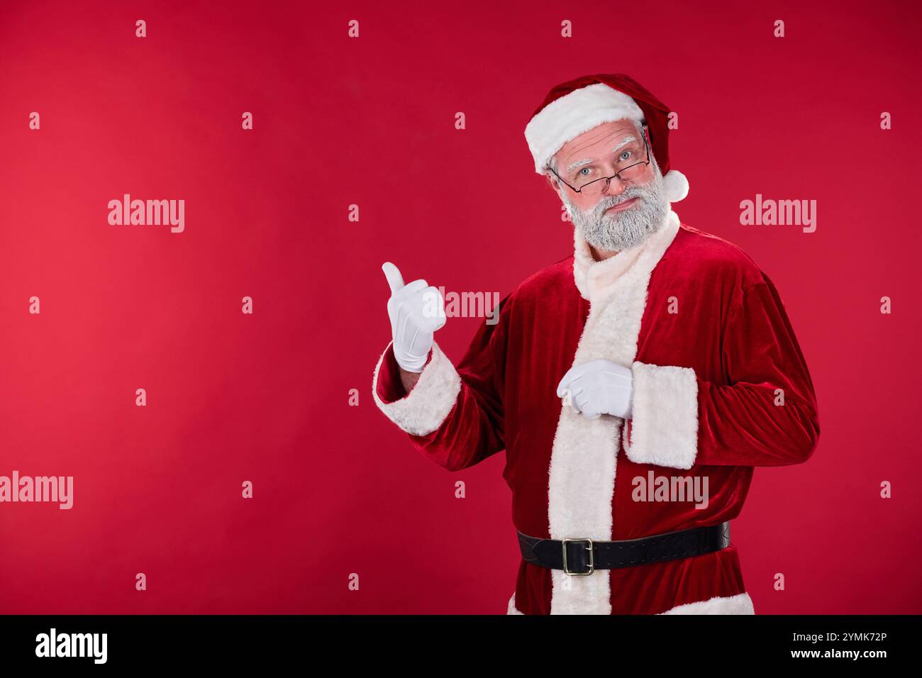 Porträt eines älteren Mannes, der als Weihnachtsmann gekleidet ist, der die Hand mit Daumen nach oben zeigt, festliches rot-weißes Kostüm und Brille trägt, die Zustimmung zur Geste gibt und fröhlich aussieht Stockfoto