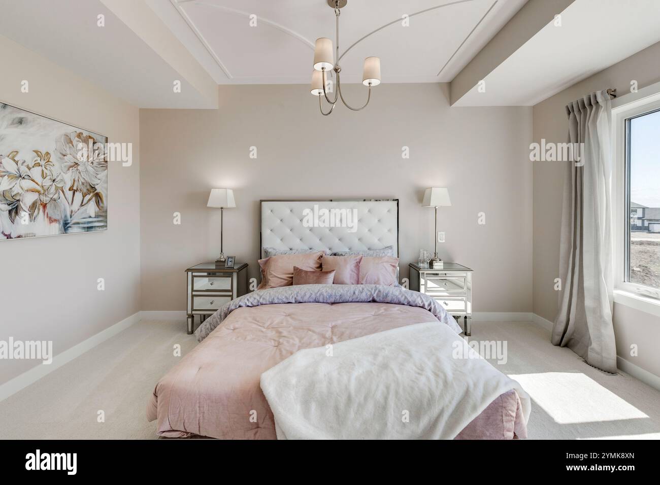 Ein Schlafzimmer mit einem weißen Bett und einer rosa Decke. Das Bett ist von zwei Nachttischen und einer Lampe umgeben. Das Zimmer hat ein sauberes und einfaches Design, mit einem weißen Stockfoto