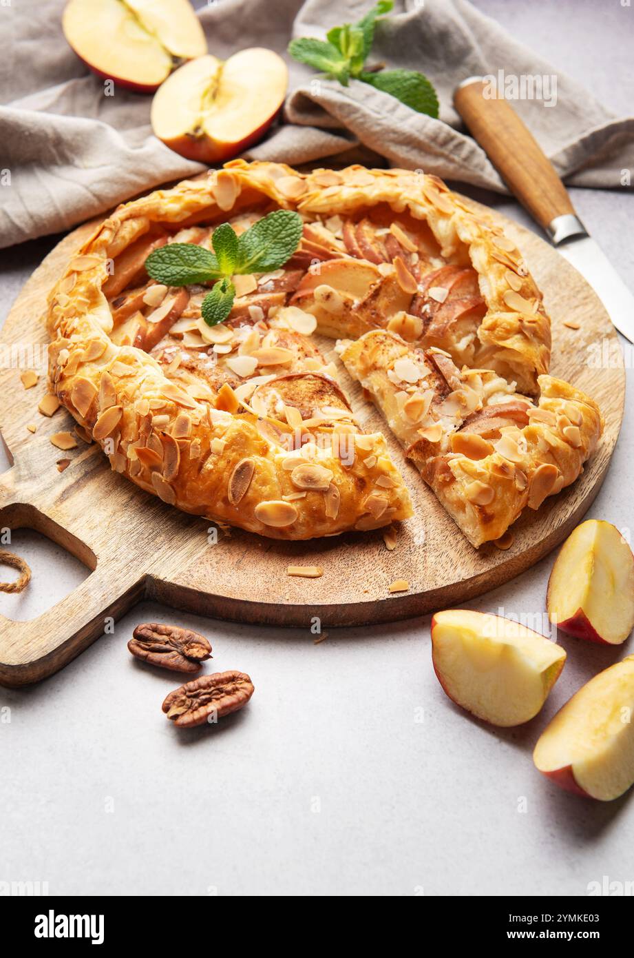 Frisch gebackene Apfelgalette, dekoriert mit Mandelflocken und Minzblättern, serviert auf einem Holzbrett Stockfoto