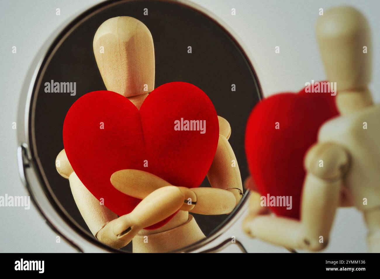 Hölzerne Schaufensterpuppe mit Herz, das sich selbst im Spiegel betrachtet - Love Yourself Konzept Stockfoto
