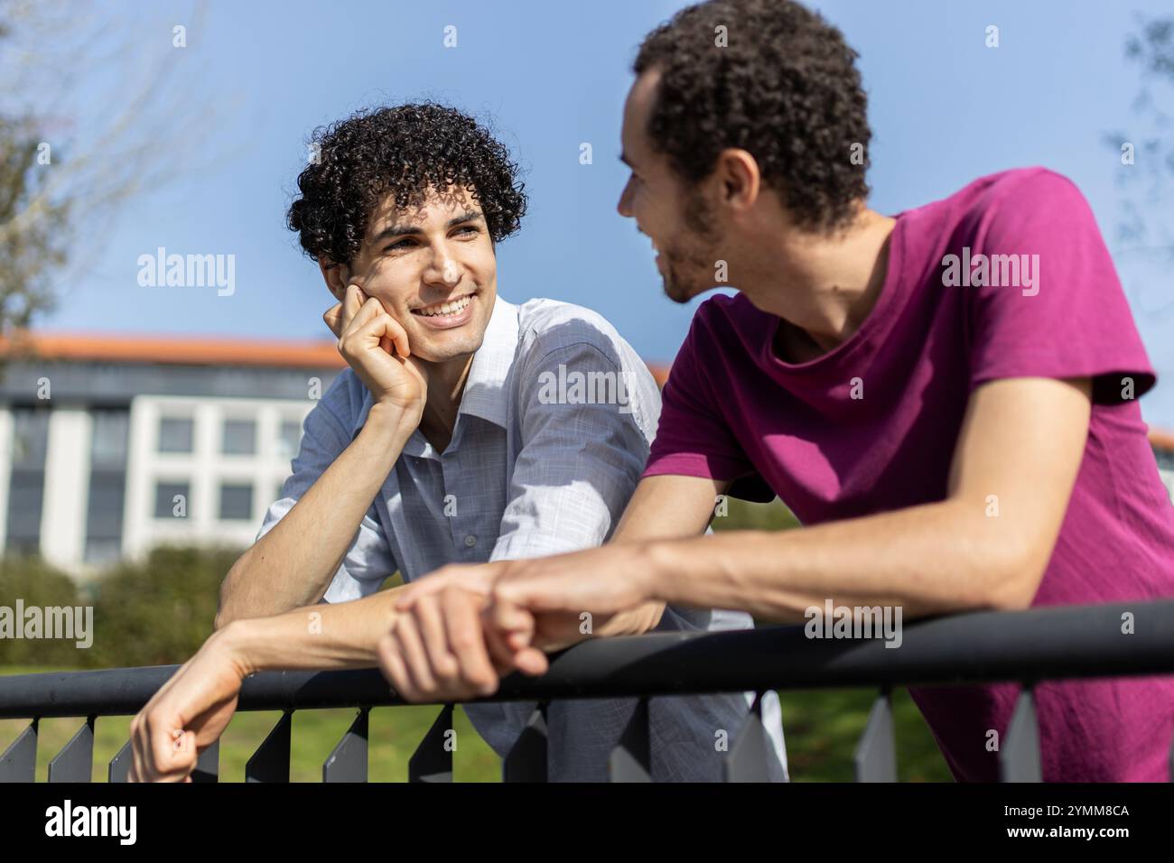 Zwei Männer, ein schwules Paar, genießen einen sonnigen Tag, lehnen sich auf ein Geländer und reden Stockfoto