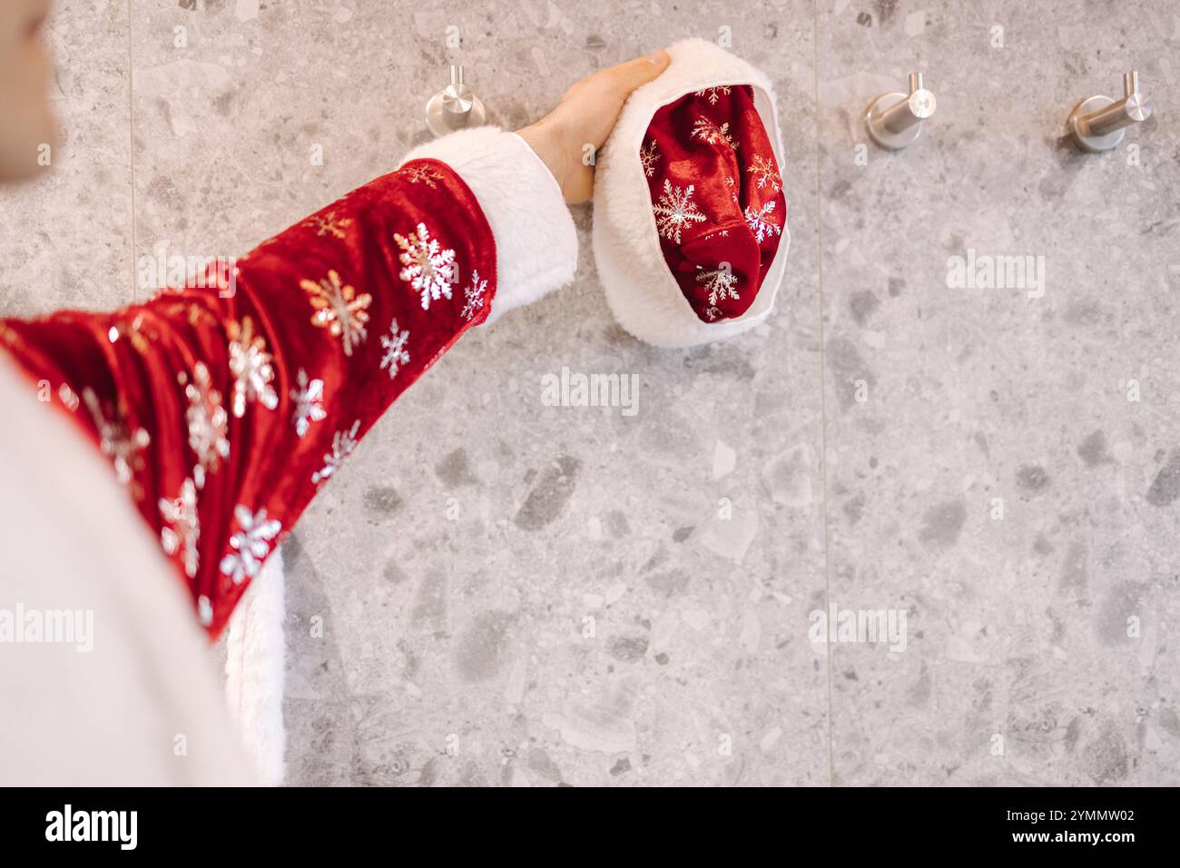 Nahaufnahme der Hand des Weihnachtsmanns in einem festlichen Gewand, der einen Hut an einem Wandhaken verstellt und praktische und weihnachtliche Atmosphäre kombiniert. Stockfoto