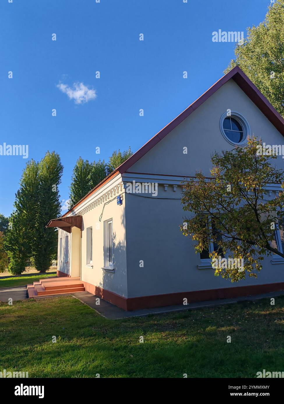 Stabiles Gebäude mit roten Ziegelsäulen und einem schrägen Dach, vor einem blauen Himmel und grünen Bäumen. Die Struktur vermittelt zeitlose architektonische Werte Stockfoto