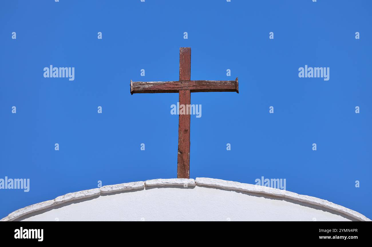 Altes christliches Kreuz aus braun verwittertem Holz auf einem weißen Bogendach Stockfoto
