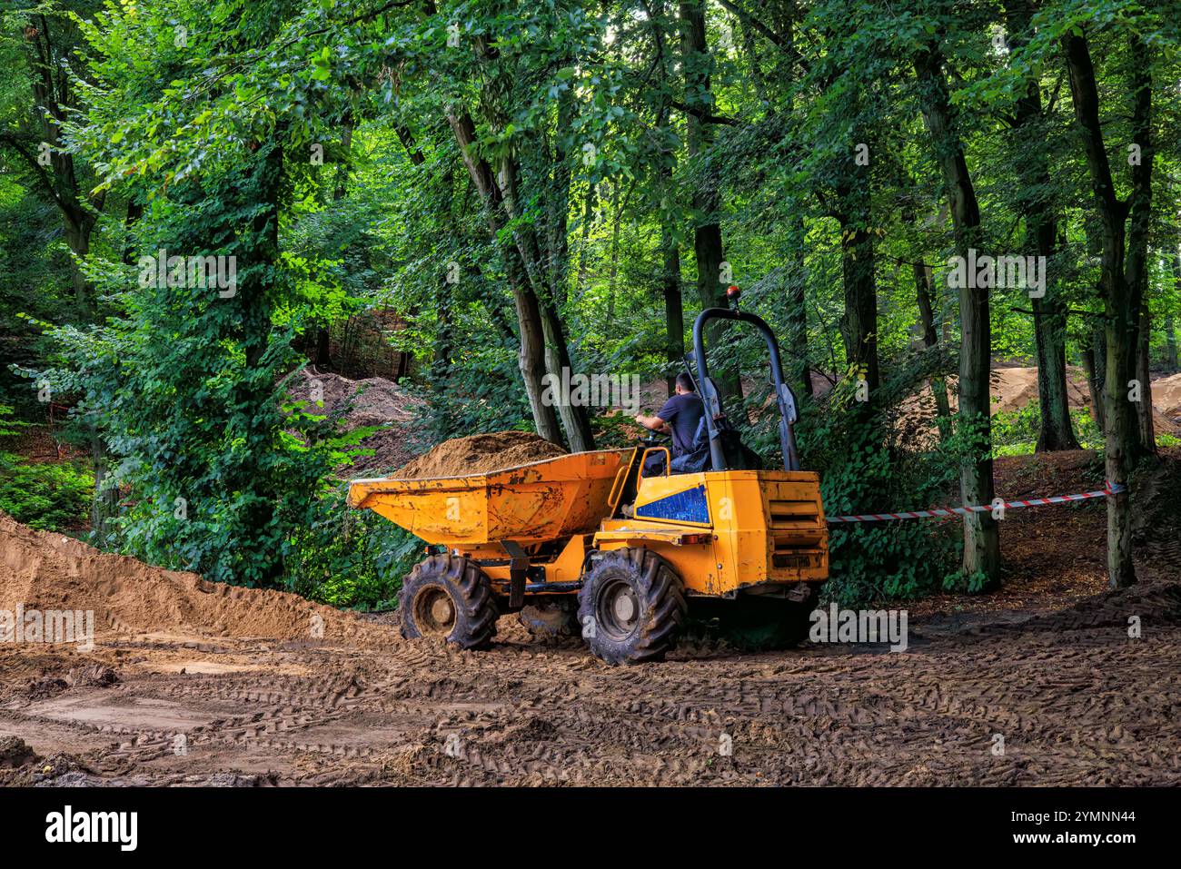 Ein kleiner oranger Baukipper entfernt Erde von einer Baustelle in einem Park. Stockfoto