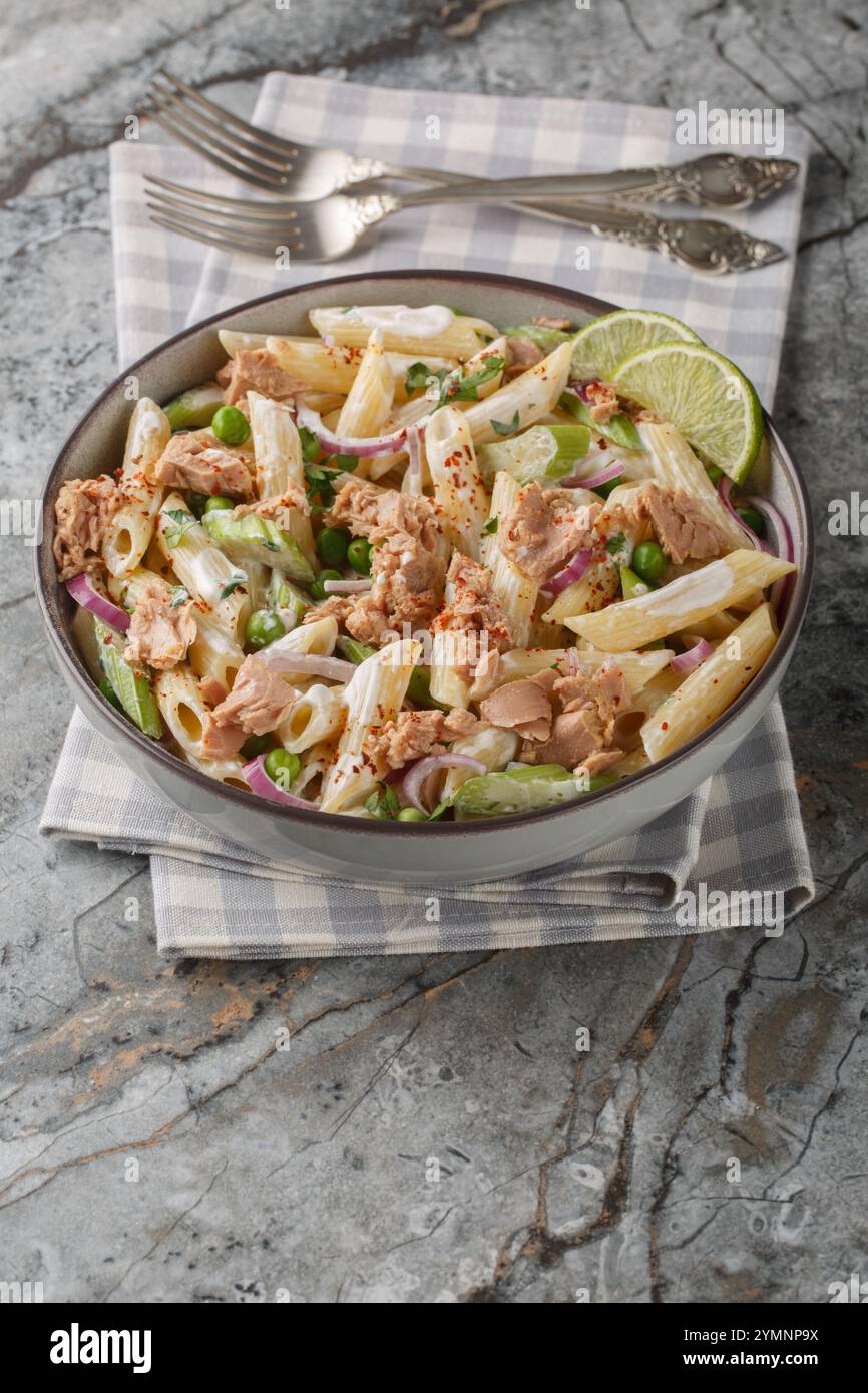 Cremiger Thunfisch-Pasta-Salat mit grünen Erbsen, Zwiebeln, Sellerie und Joghurtdressing auf dem Teller auf dem Tisch. Vertikal Stockfoto