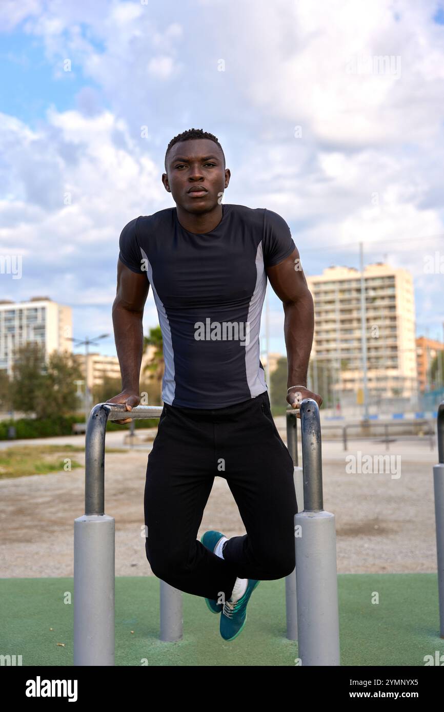 Junger schwarzer Mann, der Calisthenics-Dips an parallelen Bars im Stadtpark durchführt Stockfoto