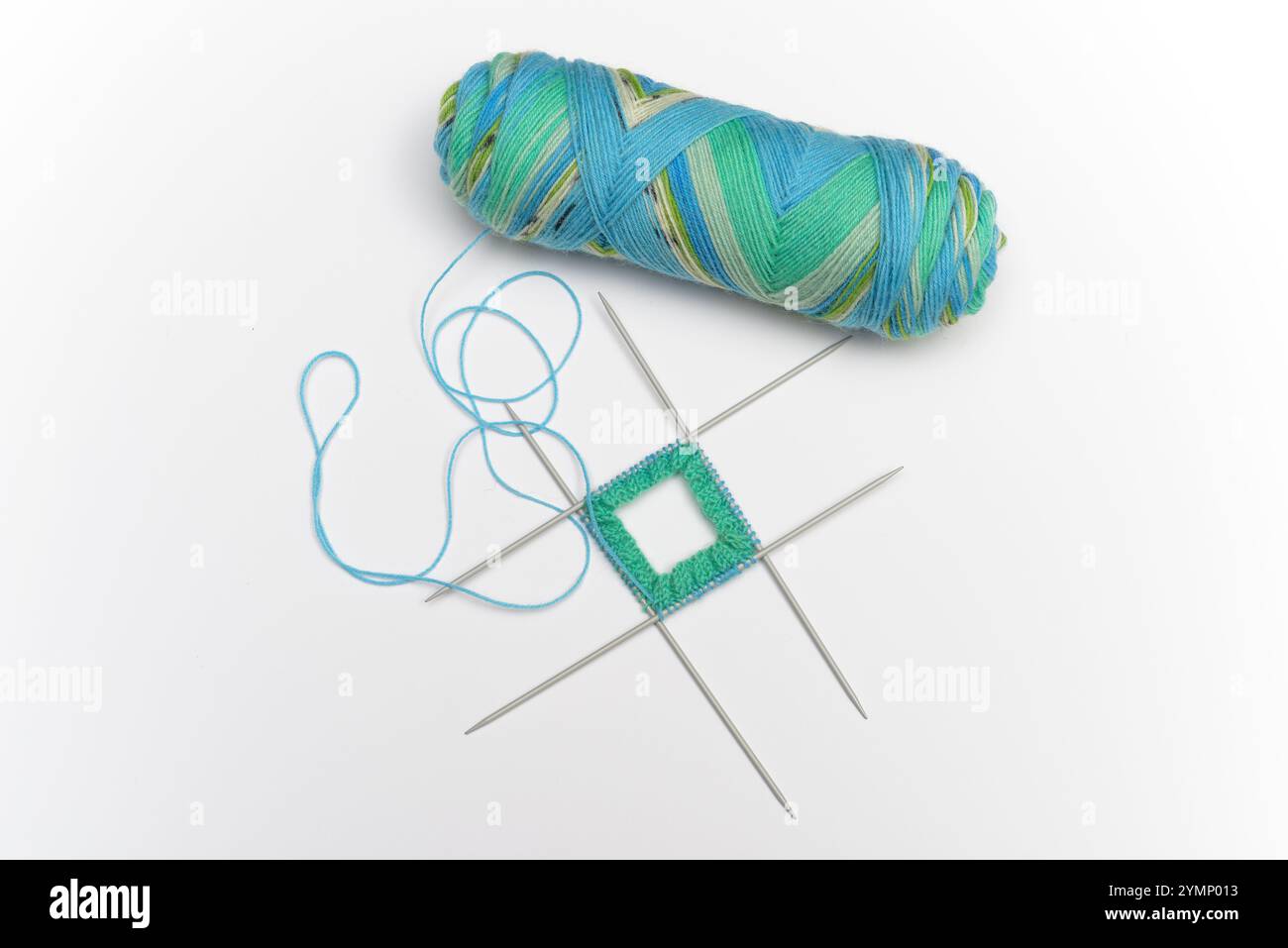 Ein Knäuel aus buntem, buntem Garn in Blau-, Grün- und Gelbtönen, zusammen mit einem kleinen Strickprojekt auf vier doppelzackigen Nadeln. Das Proje Stockfoto