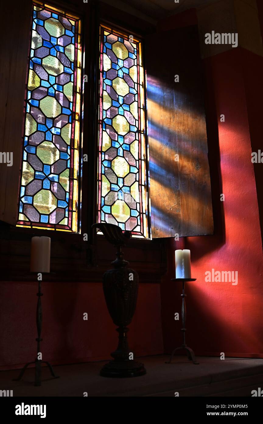 Ein Buntglasfenster in einer spanischen Burg, mit Sonnenlicht und einer Kerze, die diesem historischen Meisterwerk einen warmen Glanz verleiht. Stockfoto