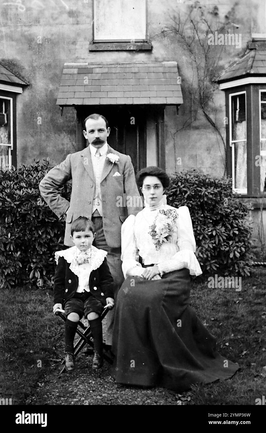 Ein Familienfoto nach einer Hochzeit. Der Mann steht mit einer Knopflochblume in der Jacke, die Dame sitzt mit einem raffinierten Blumenarrangement auf ihrer Bluse. Der Junge sitzt auch. Das Originalfoto stammt aus der Zeit um 1920 und wurde von der Redhill Photo Co der Station Road, Redhill, Surrey, England, aufgenommen. Stockfoto