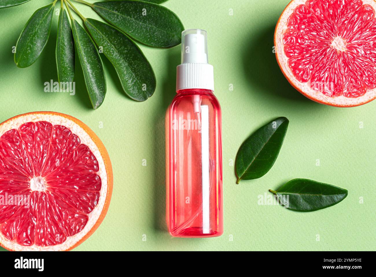 Körpernebelspray, Gesichtsnebelflasche mit Grapefruits und grünen Blättern auf grünem Hintergrund. Naturkosmetik mit Zitrusfruchtextrakt. Zitrusfrüchte Stockfoto