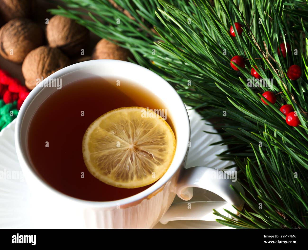 Eine Tasse Morgentee mit Zitrone und Walnüssen vor dem Hintergrund grüner Zweige eines Weihnachtsbaums. Dekorationen für Neujahr und Weihnachten. A Stockfoto