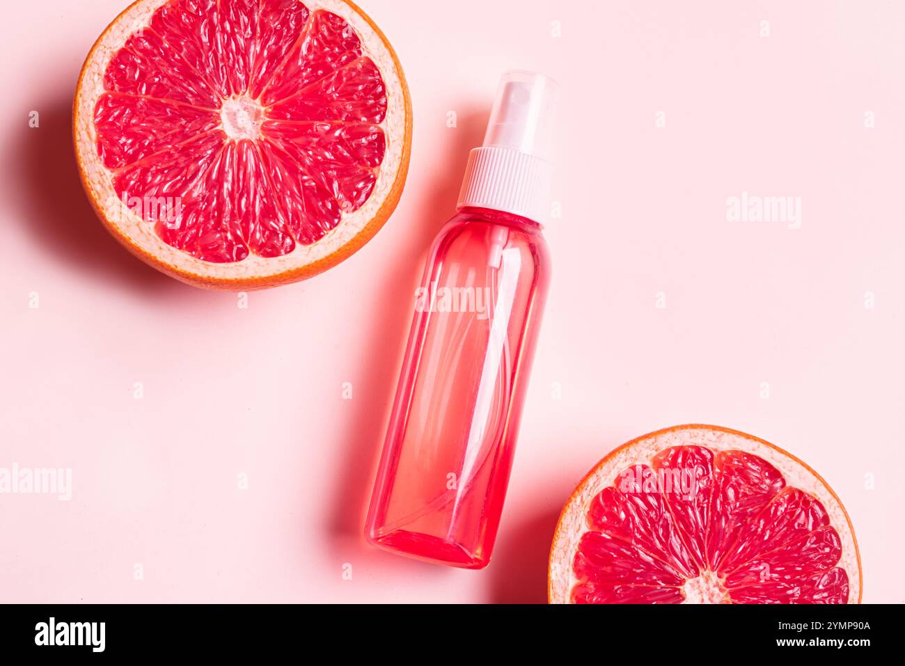 Körpernebelspray, Gesichtsnebelflasche mit Grapefruitscheiben auf rosa Hintergrund. Naturkosmetik mit Zitrusfruchtextrakt. Ätherisches Zitrusöl, Stockfoto